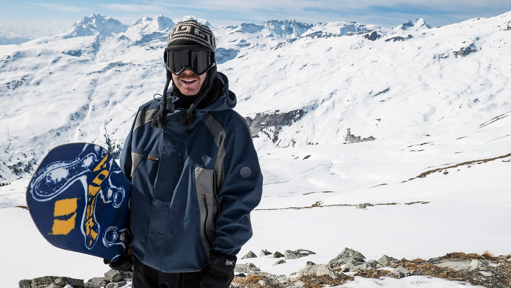 Armada Snowboard athlete, Alex Oestreng, holding a snowboard in the mountains.