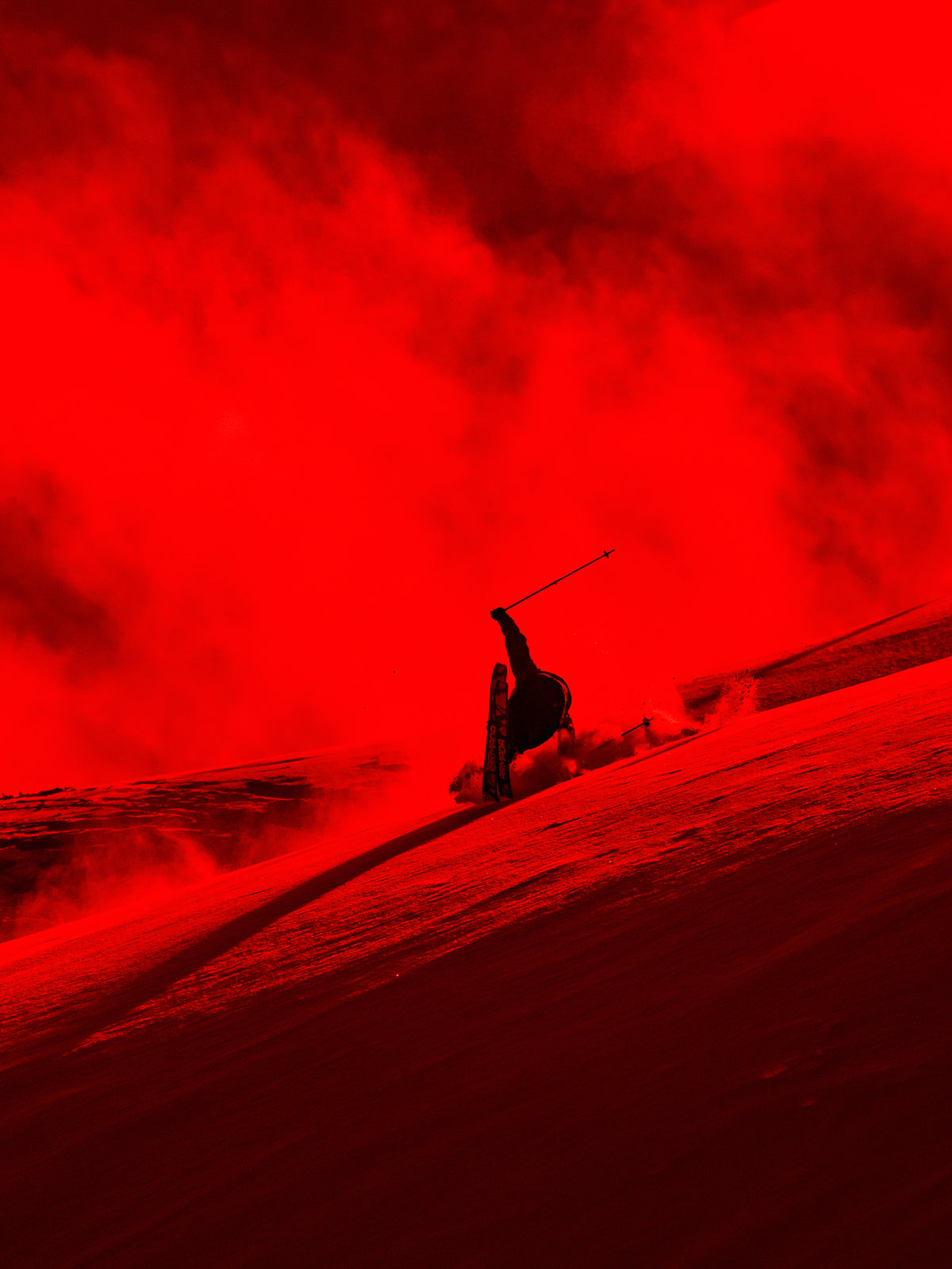 A dramatic red-tinted action shot of a skier carving through powder on a snowy slope, with a dark silhouette and a large smoky red area in the background.